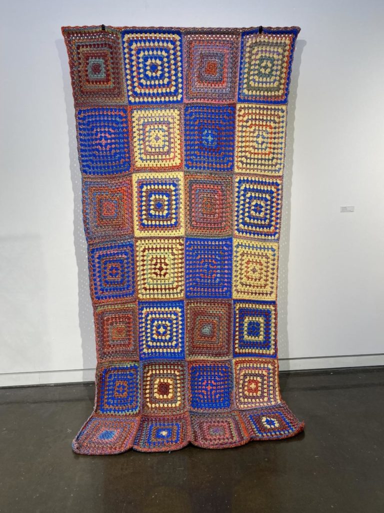 A large crochet quilt made of granny squares of various patterns, all using yellow, orange, and blue yarn